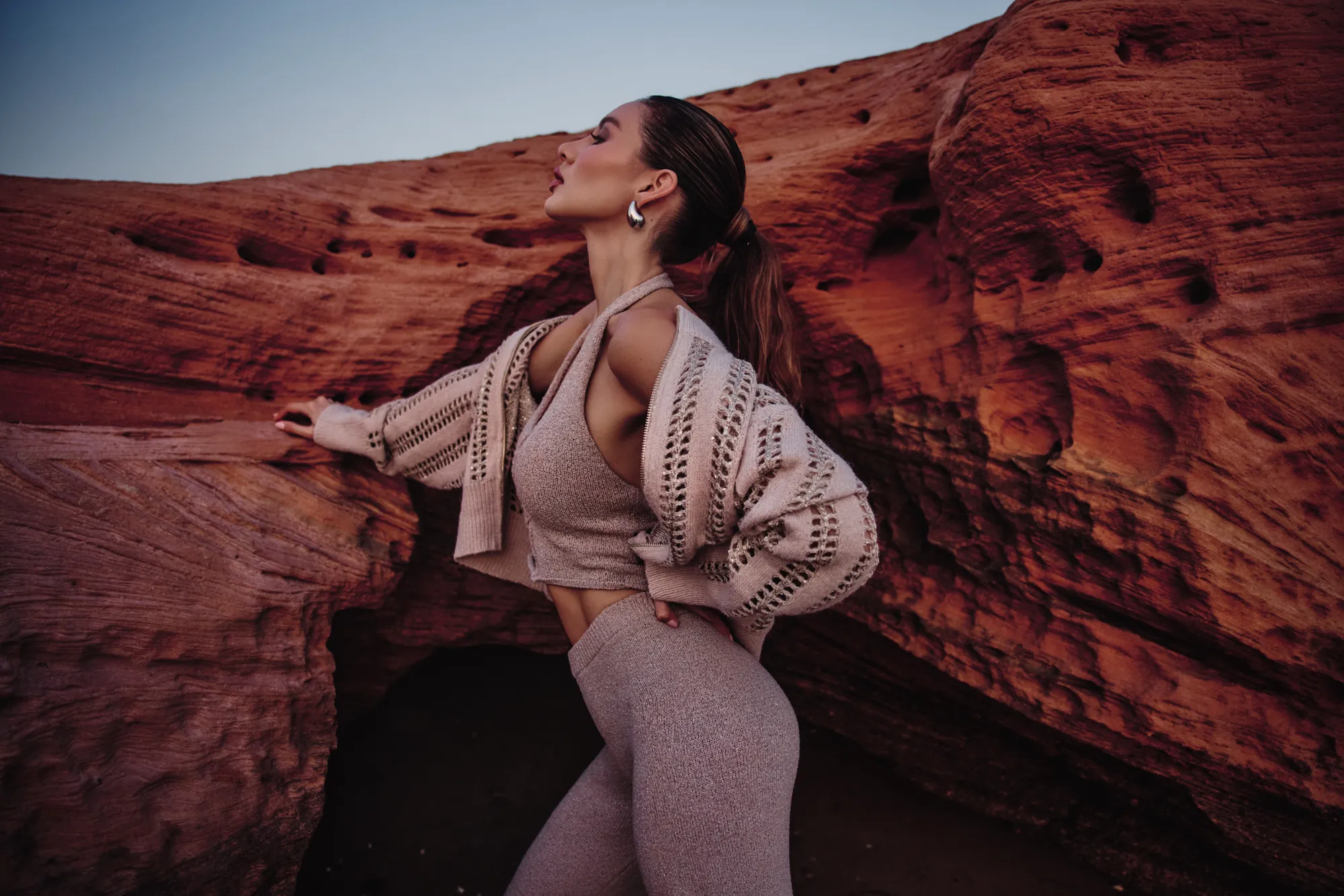 Model in profile in a taupe knit halter set and open-knit cardigan, palm pressed to a red canyon wall